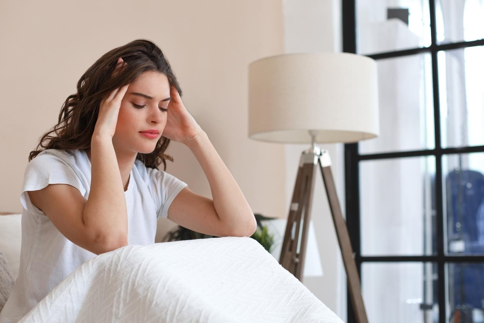 Sleeping Pill Abuse: Risks & Withdrawal 2 beautiful young woman sitting in bed suffering headache massaging her head with eyes closed